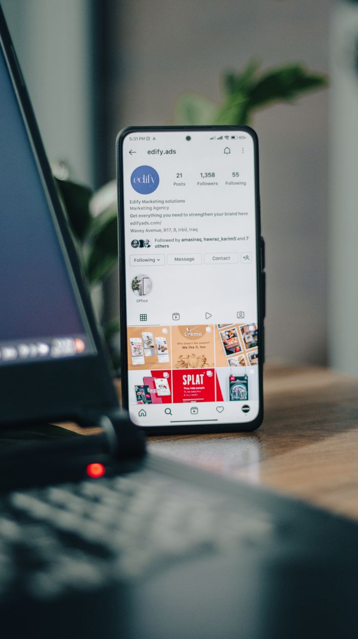 how-we-are Vertical shot of a smartphone displaying an Instagram profile next to a laptop, representing social media engagement.